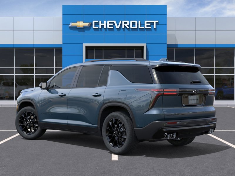 Vue arrière trois quarts d’un Chevrolet Traverse bleu-gris devant une concession Chevrolet, mettant en valeur les feux arrière DEL, les jantes noires et le design robuste et spacieux du VUS familial moderne.